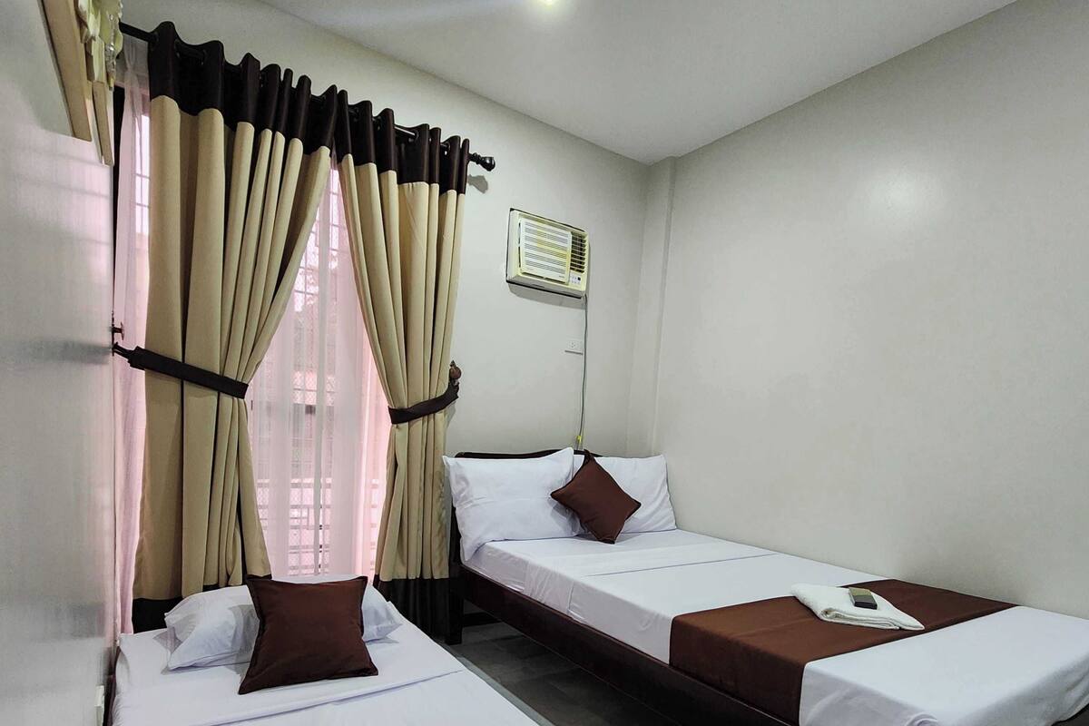 Een hotelkamer met twee eenpersoonsbedden, een nachtkastje met een afstandsbediening en een airconditioner aan de muur.