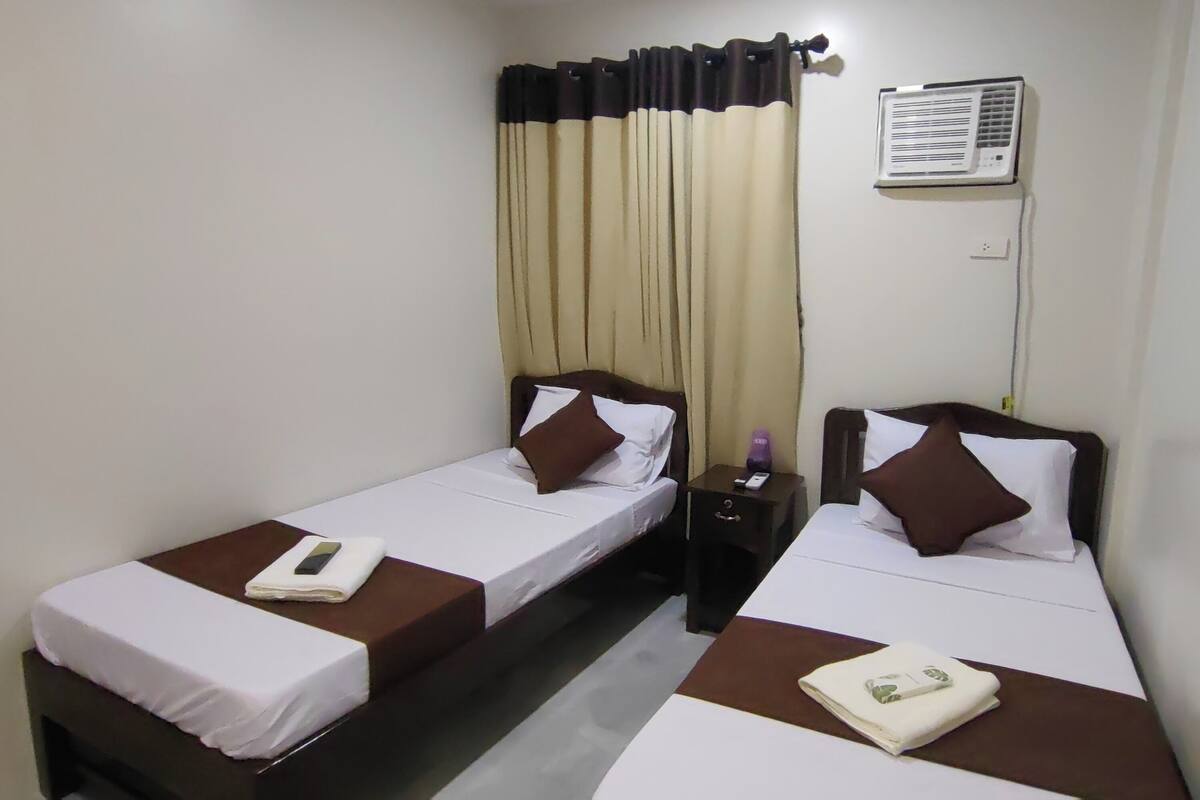 Een hotelkamer met twee eenpersoonsbedden, een nachtkastje met lamp, een airconditioning en een gordijn.