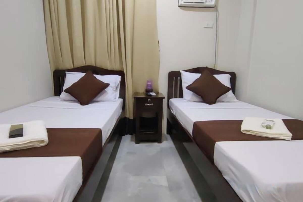A hotel room with two single beds, a nightstand, a lamp, and a window with curtains.