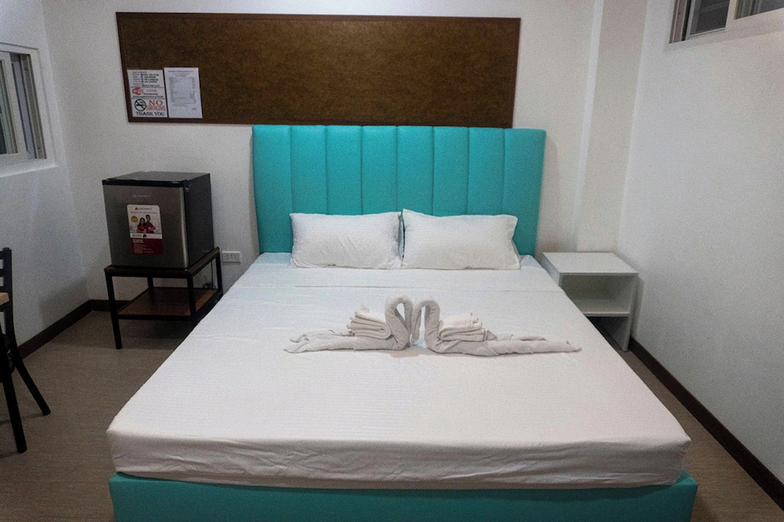 Quarto de hotel com cama, mesa de cabeceira, mesinha e uma cadeira.