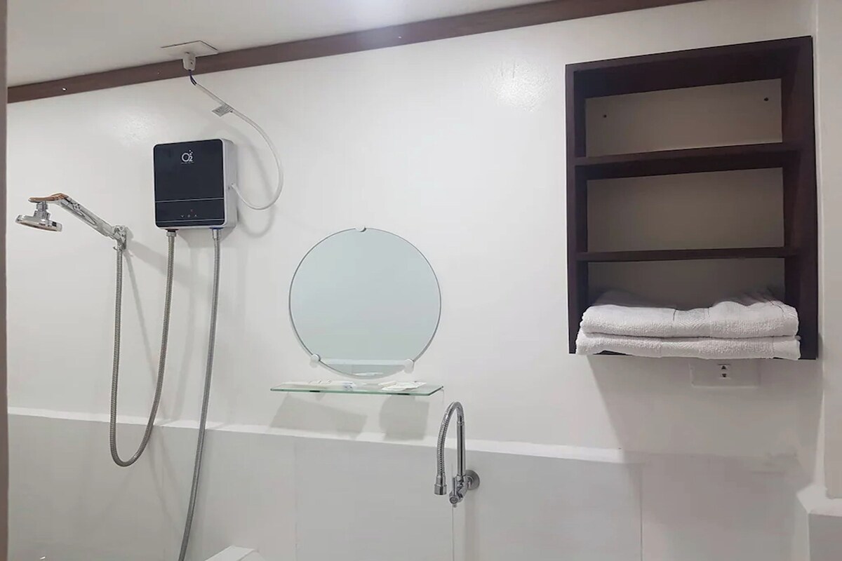 A bathroom with a glass-enclosed sink, a round mirror, a towel rack, and a shower unit.