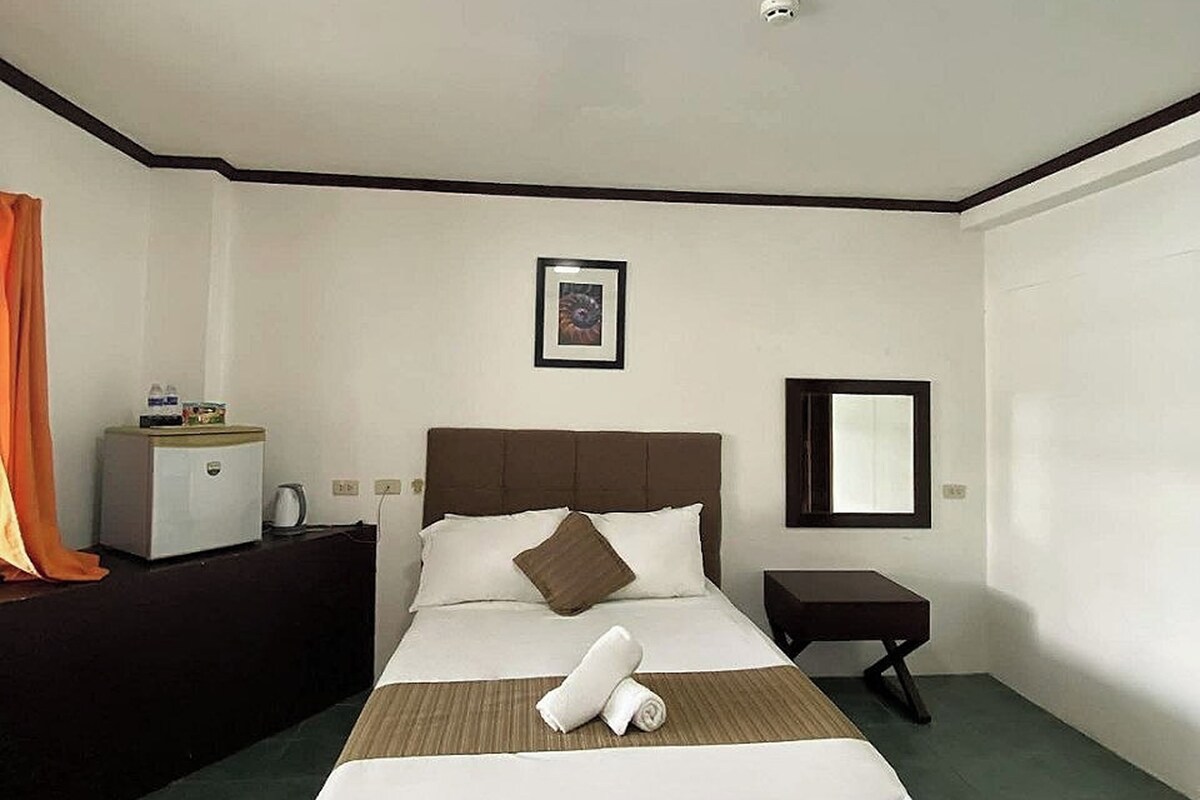 A hotel room with a bed, a bedside table, a nightstand, a mirror, and a picture on the wall.