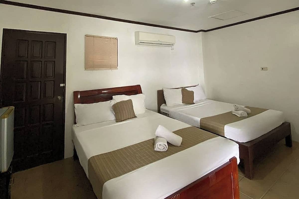A hotel room with two beds, a wooden door, an air conditioning unit, and a tiled floor.