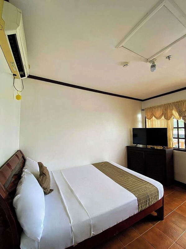 A hotel room with a bed, a TV, a desk, and a window with curtains. - Subiza Beach Resort (Olongapo)