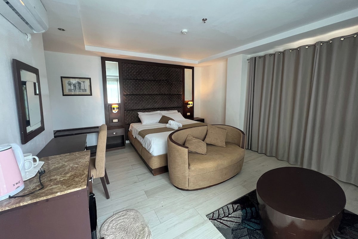 A modern hotel room with a bed, a sofa, a desk, and a coffee maker.