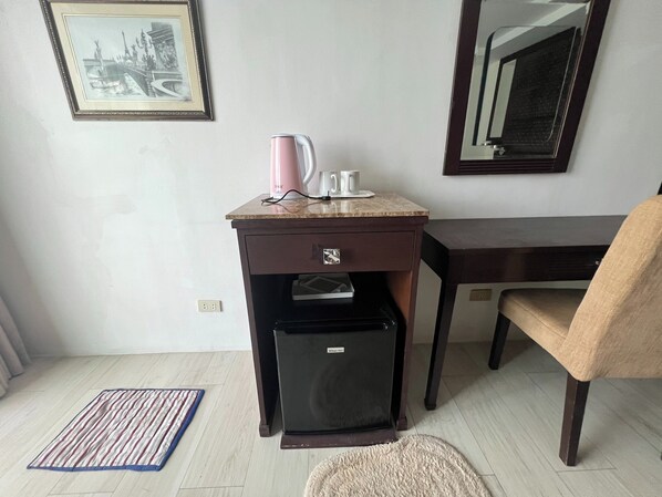Une pièce de taille modeste comprenant un bureau, une chaise, un petit réfrigérateur et une machine à café.