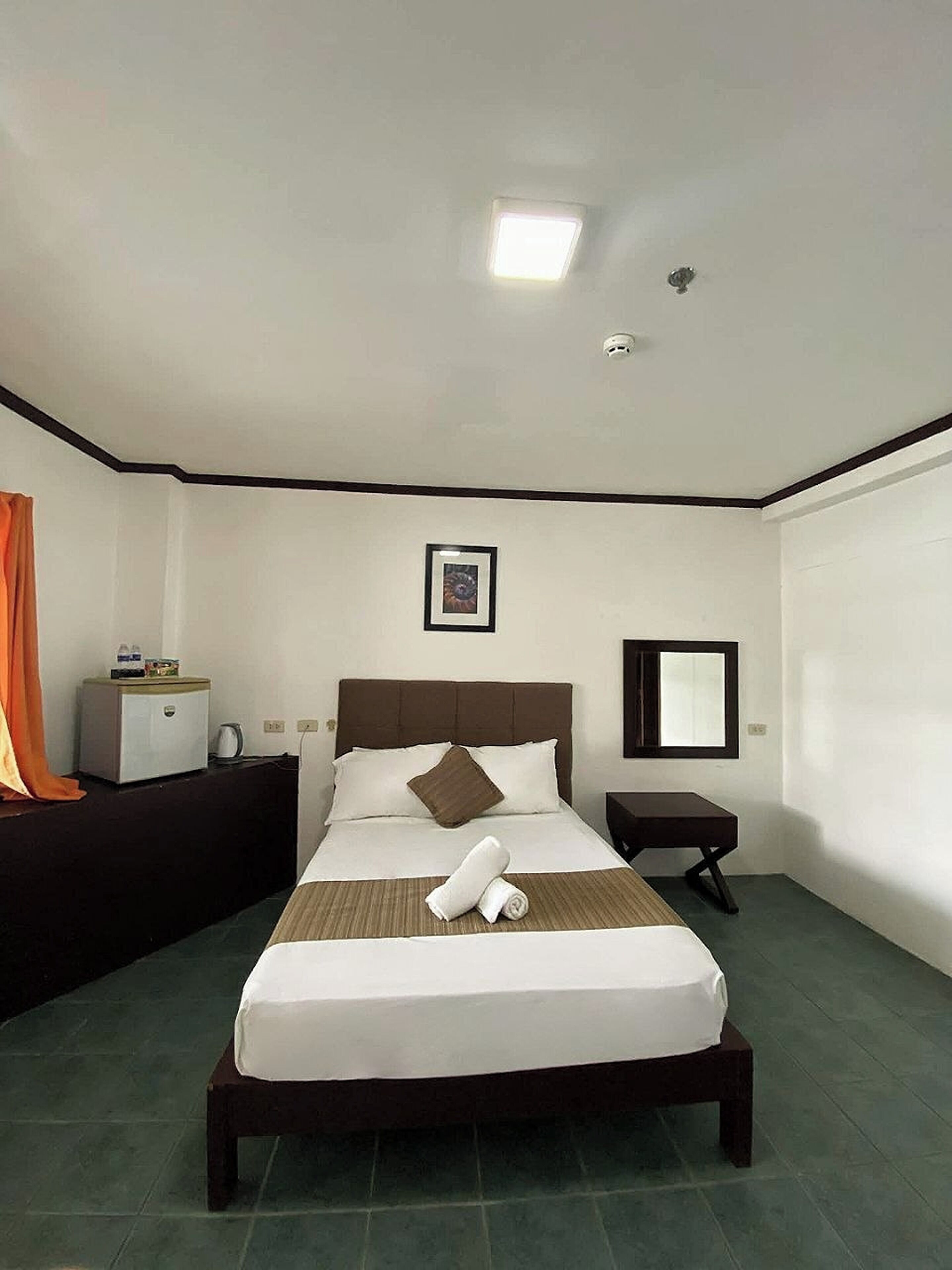 Habitación de hotel con cama, mesita de noche, espejo y un cuadro en la pared.