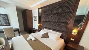Hotellihuone, jossa on suuri sänky, työpöytä, tuoli ja peili.