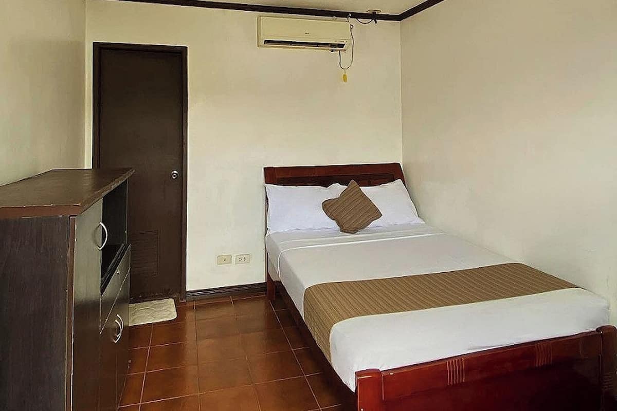 A bedroom with a bed, a dresser, a door, and a ceiling light fixture.