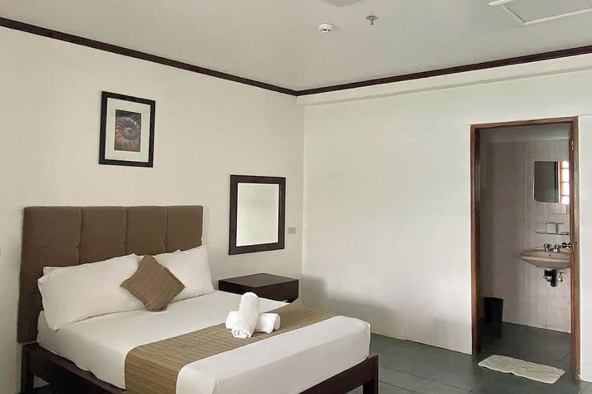 A hotel room with a bed, a bedside table, a mirror, and a door leading to a bathroom.