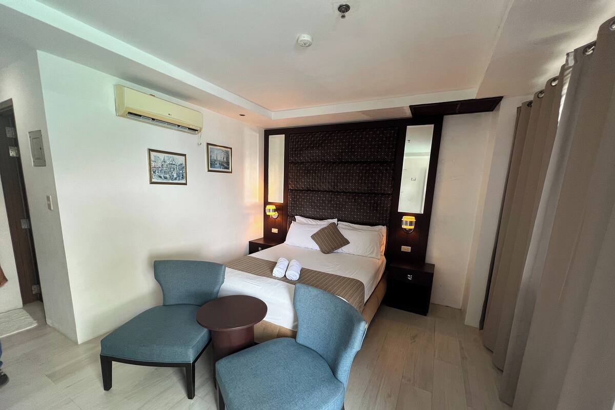 A hotel room with a bed, two armchairs, a small table, and a nightstand.