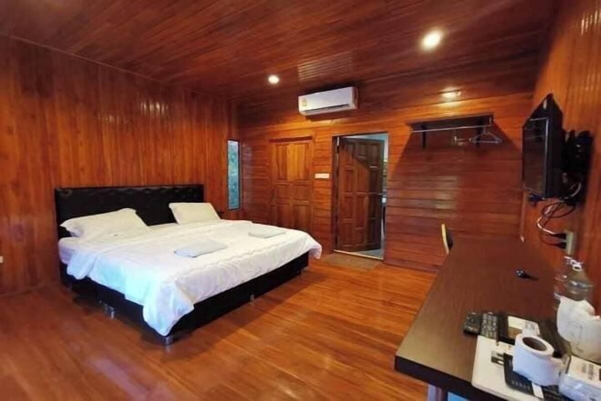 Ein Zimmer mit Holzwänden, einem Bett, einem Schreibtisch mit Computer und einer Klimaanlage.