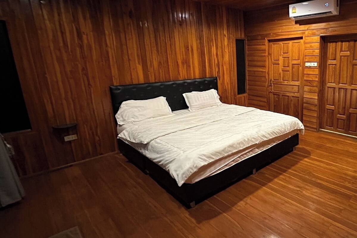 Ein Zimmer mit Holzwänden, einem Bett, Holzdielen und einer Tür.