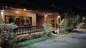 Un bâtiment traditionnel en bois, doté de grandes fenêtres et d’un balcon, et entouré de verdure.