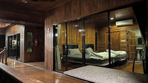 Une pièce aux murs lambrissés, un lit avec une literie verte, une petite table et une salle de bain équipée d’un lavabo et d’un miroir.