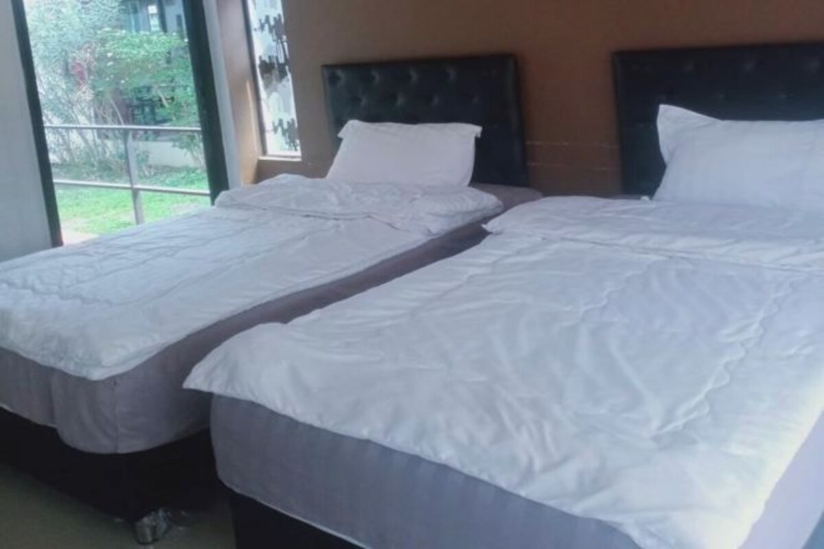 Een kamer met twee eenpersoonsbedden, een donker hoofdeinde en een raam met uitzicht op groen.