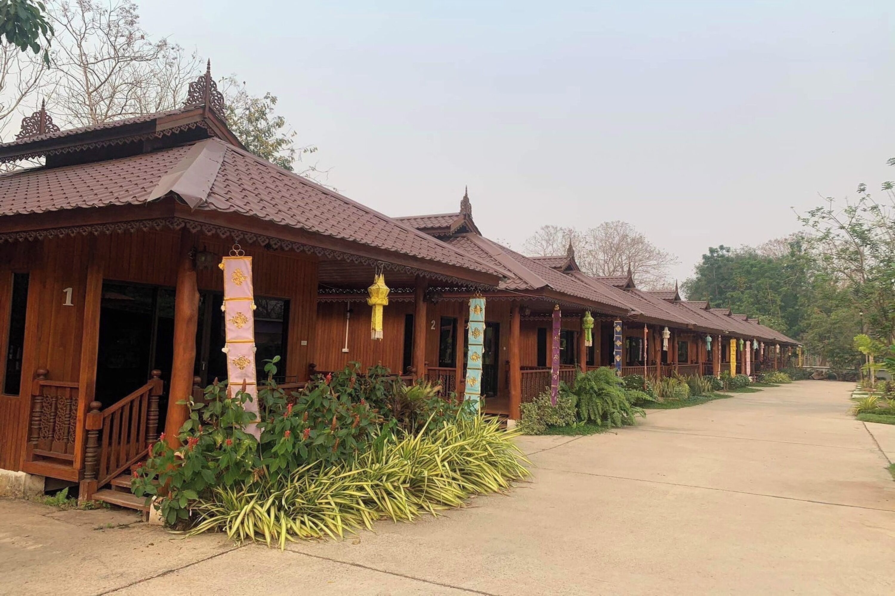 Une rangée de bâtiments traditionnels en bois, avec des toits en tuiles, une allée couverte et un jardin bien entretenu.