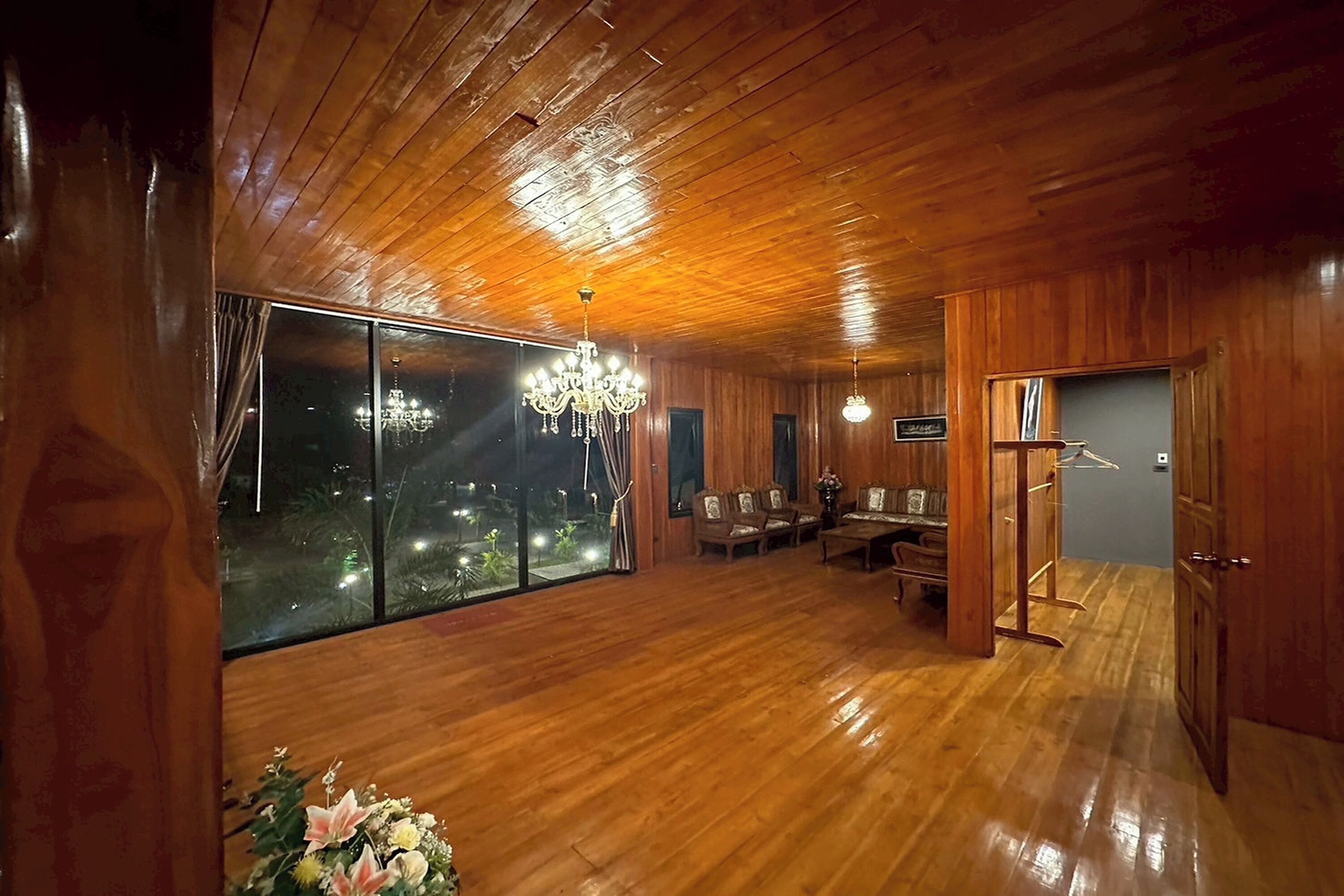 A spacious room with wooden flooring, a chandelier, large windows, and a view of the night sky.