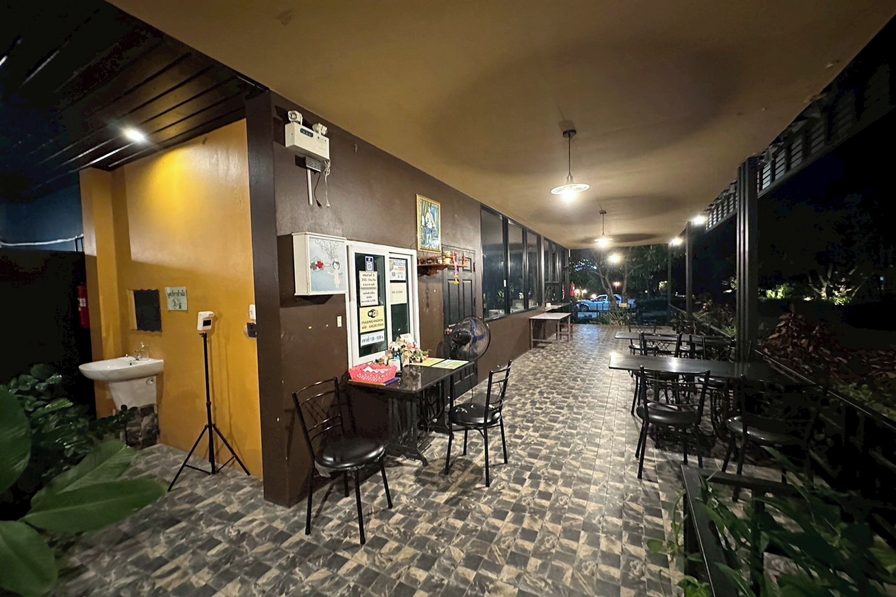 Un restaurante con suelo de baldosas, mesas, sillas, un lavamanos y un ventilador.