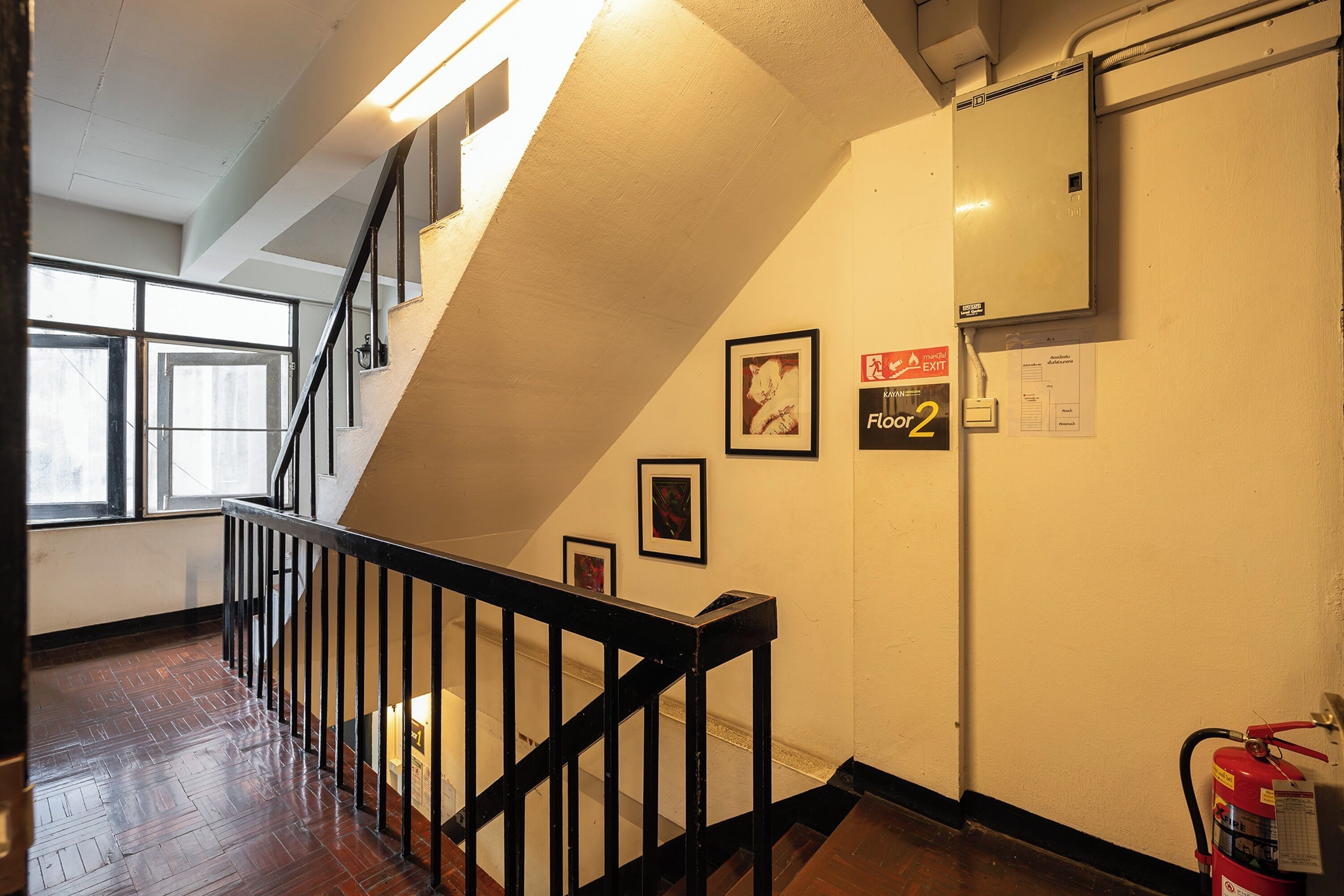 A staircase with a black railing leading to a landing, a fire extinguisher on the wall, and framed pictures on the wall.