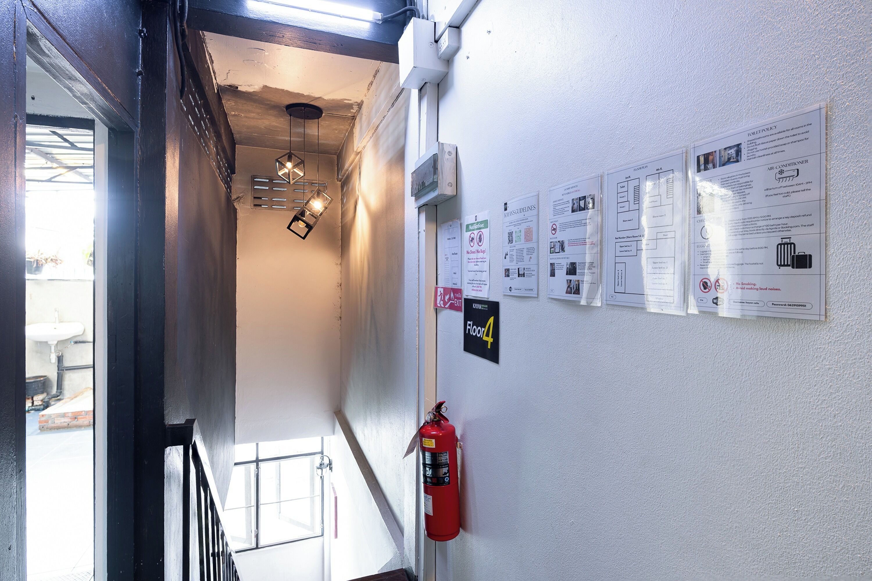 A corridor with a fire extinguisher, emergency exit sign, and informational posters on the wall.