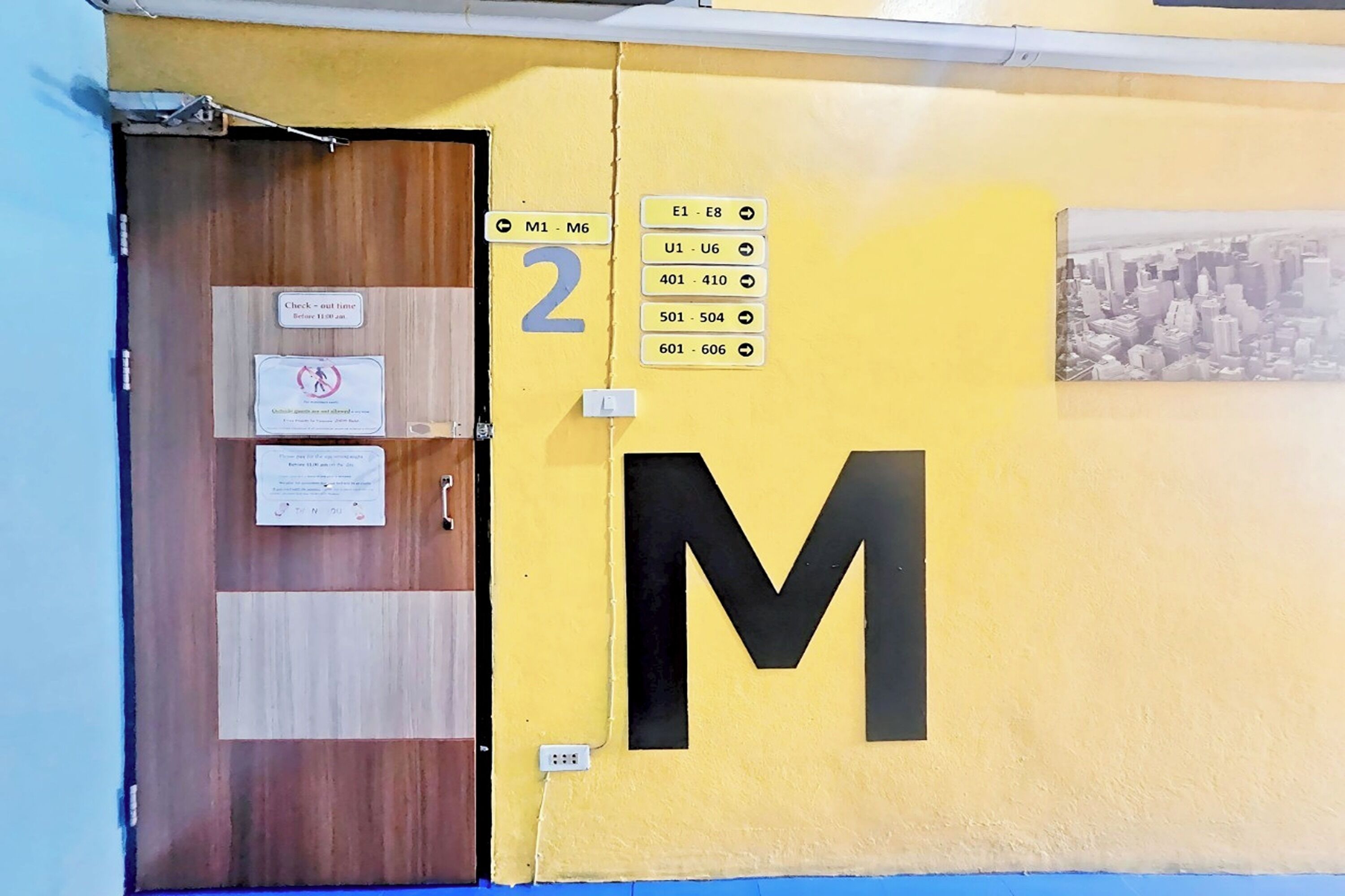 A yellow wall with a large black 'M' and room numbers 2, 3, 4, 5, 6, and 7.