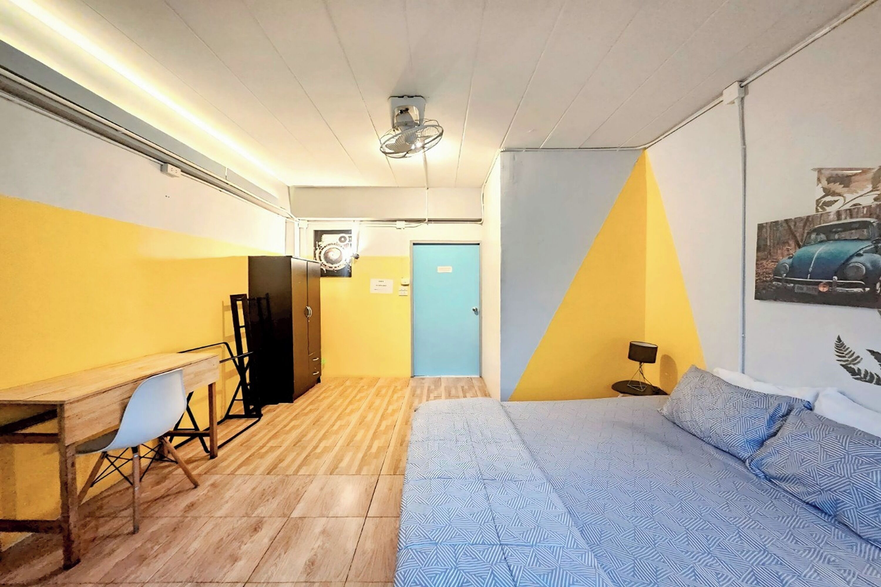 Ein Zimmer mit Bett, Schreibtisch, Stuhl, Kleiderschrank und einer Tür.