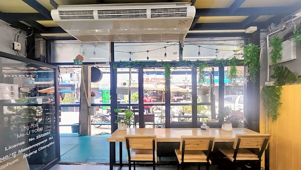 A restaurant with a large window, a table with chairs, and a green artificial grass floor. - Me U Hostel (Chiang Mai)