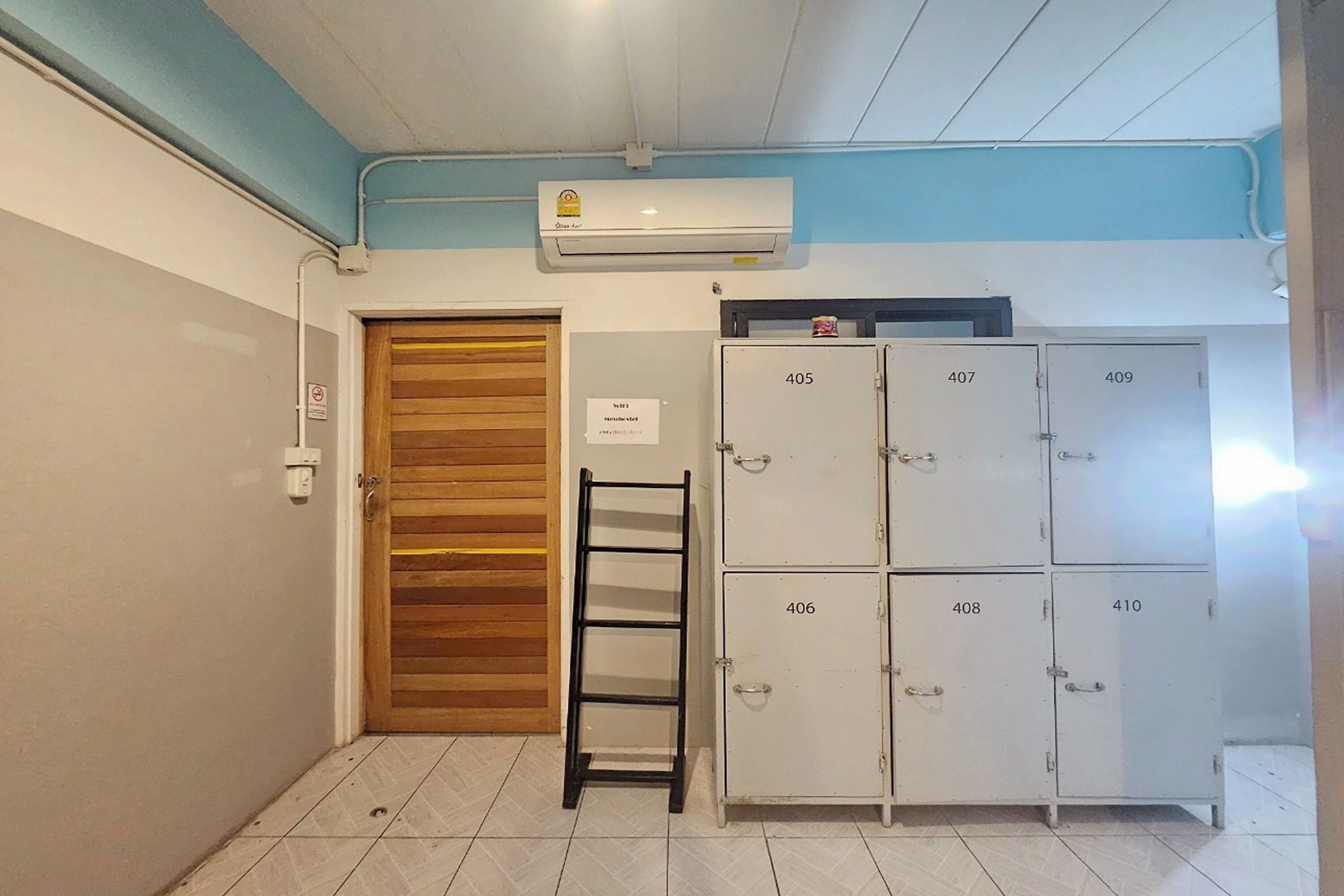 A hallway with a wooden door, a metal ladder, and a row of numbered lockers.