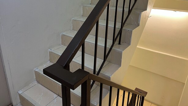 Un escalier avec une rampe noire et des marches de couleur beige.