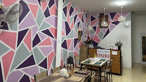Une pièce avec un mur orné d’un motif géométrique, une table avec des chaises, un ventilateur, une horloge et un panneau d’accueil.