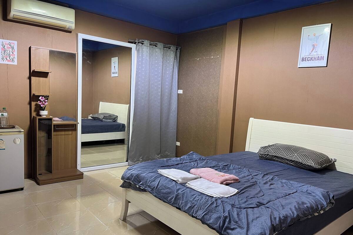 A bedroom with a bed, a bedside table, a mirror, a wardrobe, and a poster on the wall.
