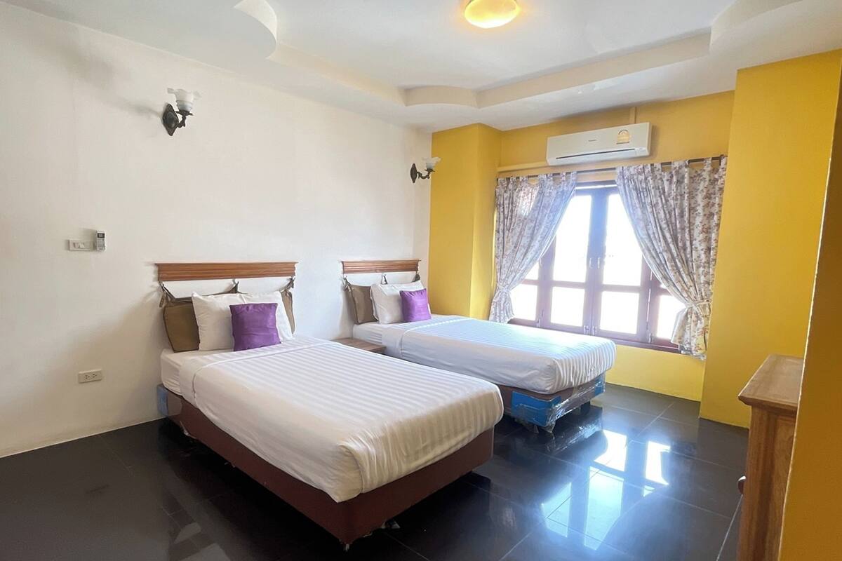 Une chambre d’hôtel avec deux lits, une fenêtre avec des rideaux, un appareil de climatisation et un luminaire fixé au mur.