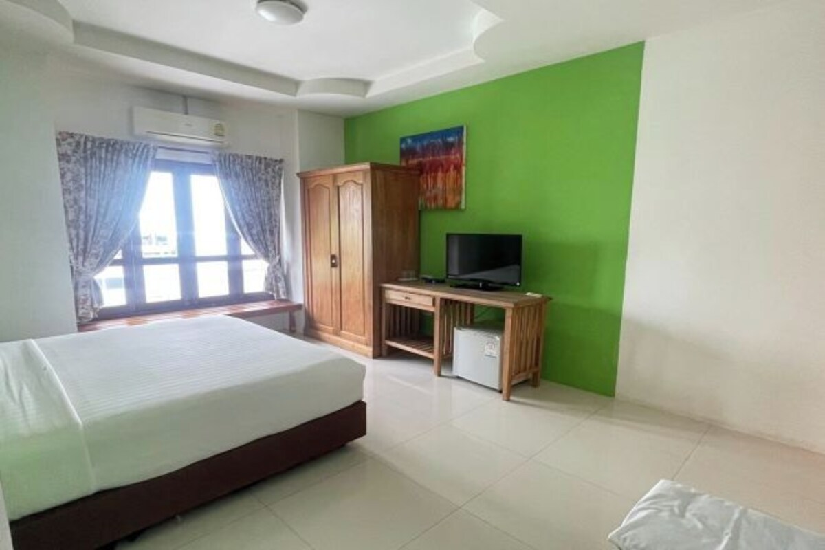 A hotel room with a bed, a desk with a television, a wardrobe, and a window with curtains.