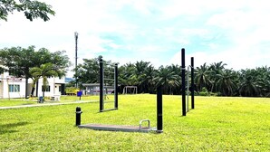 Un espacio con césped, equipamiento de ejercicio, un edificio con la leyenda 'HOUSE' y palmeras al fondo.