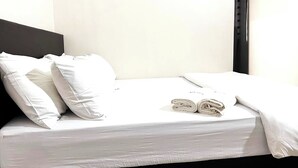 Una cama bien hecha con sábanas y almohadas blancas, una toalla enrollada sobre la cama y un cabecero negro.