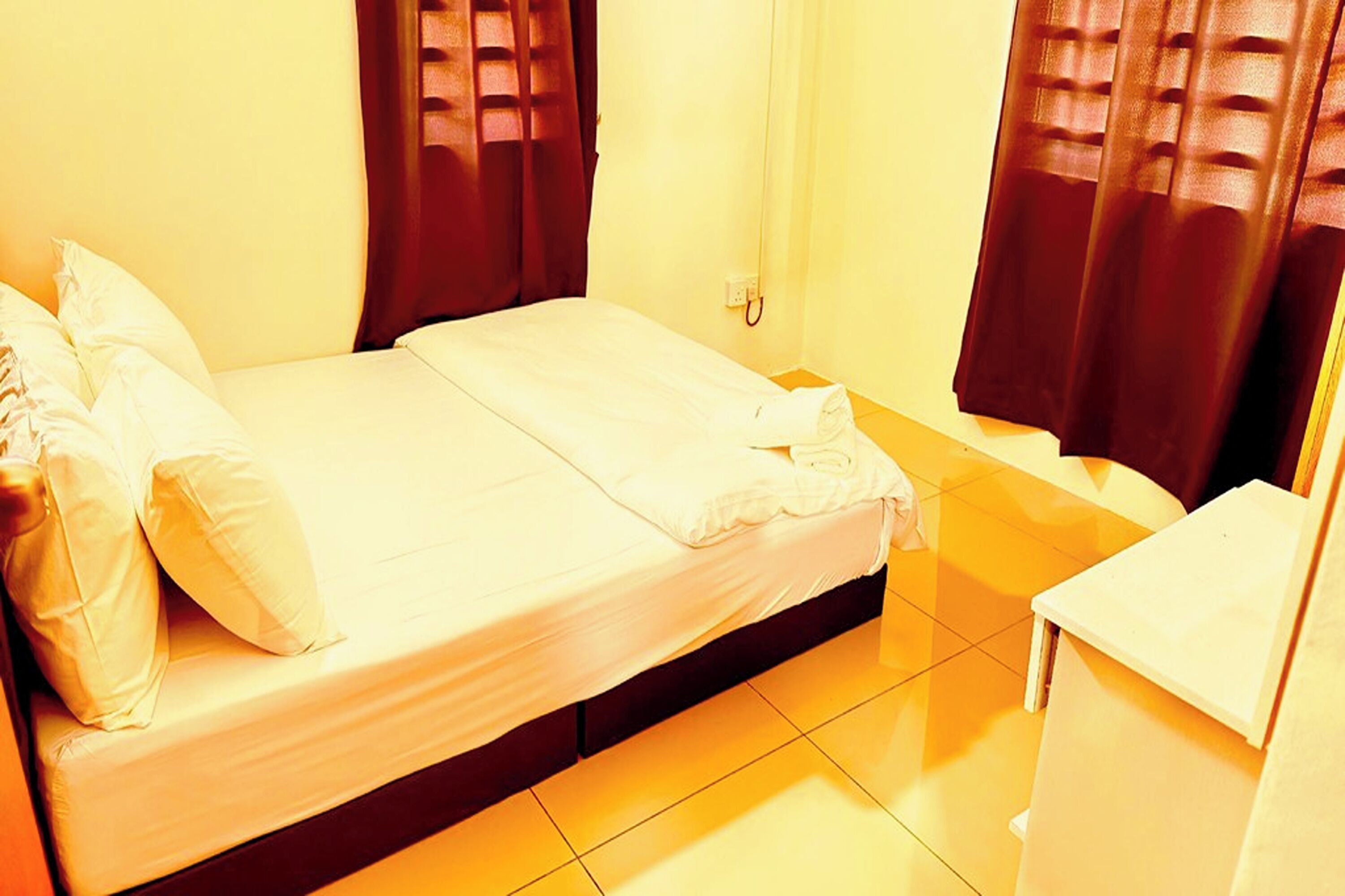 Une chambre d’hôtel avec un lit, des oreillers, une table de chevet et des rideaux.