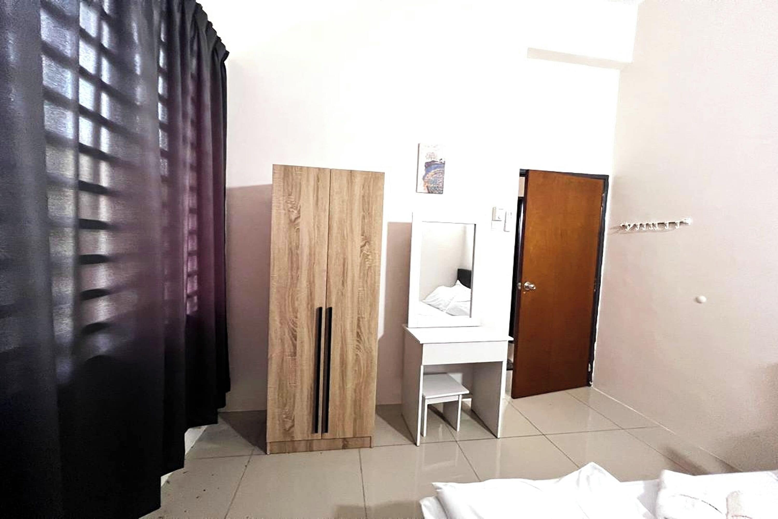 Une chambre d’hôtel avec une armoire en bois, un bureau blanc, un miroir et une porte.