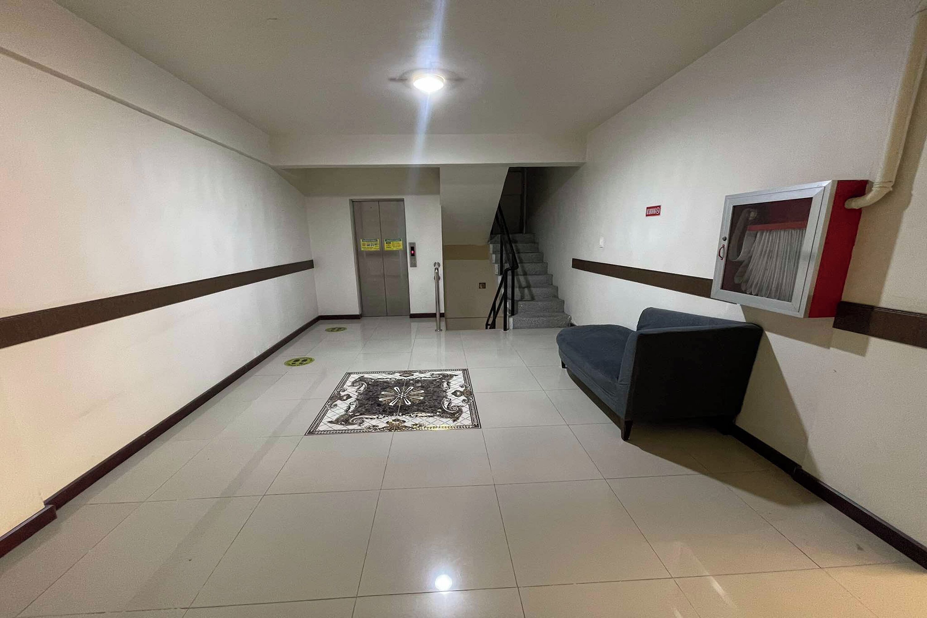 A hallway with a tiled floor, a patterned rug, a sofa, and a staircase in the background.