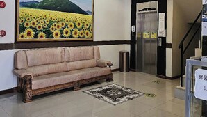 Eine Lobby mit einem großen Gemälde von einem Sonnenblume, einer Couch, einem Mülleimer und einem Aufzug.