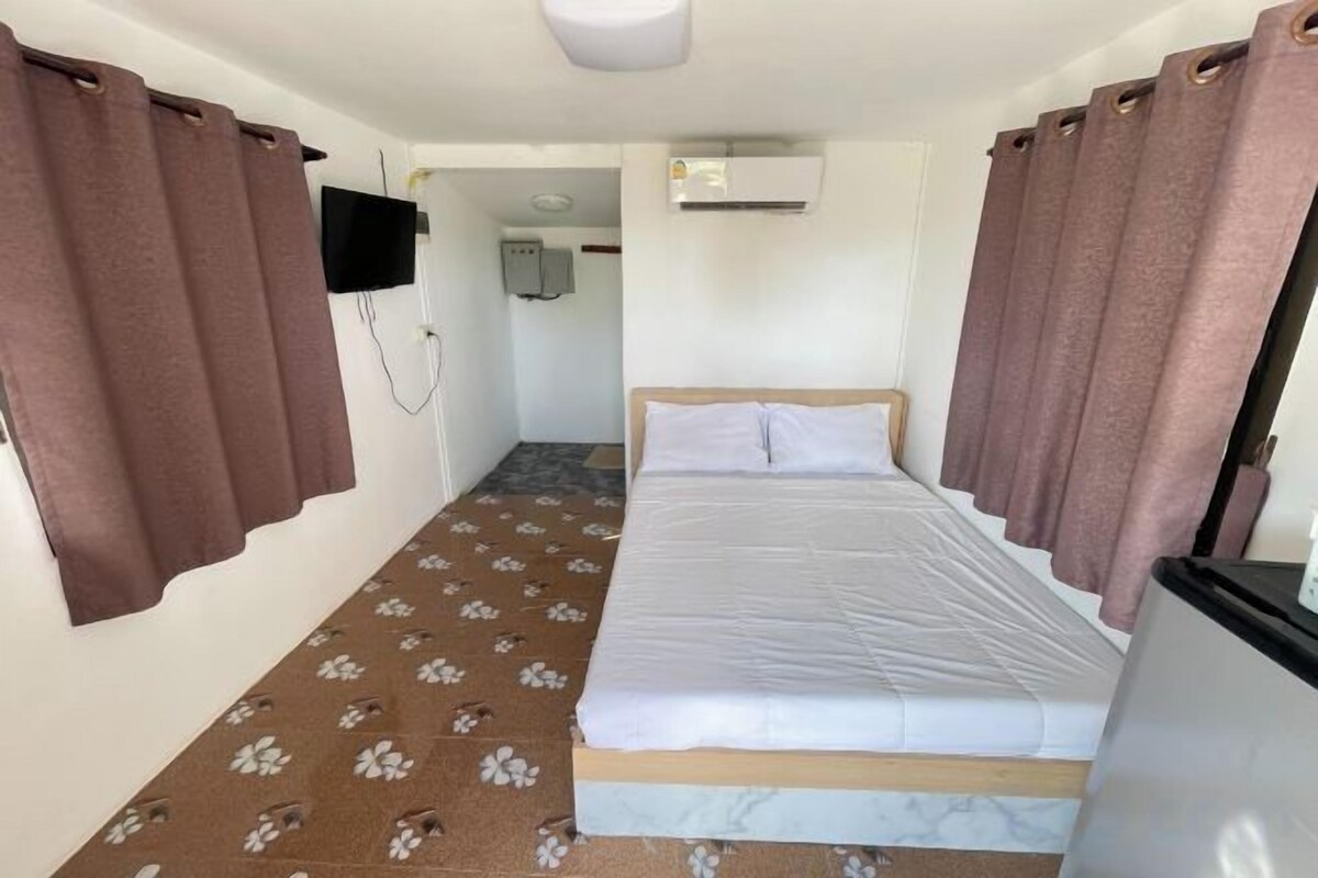 A bedroom with a bed, curtains, a television, and an air conditioning unit.