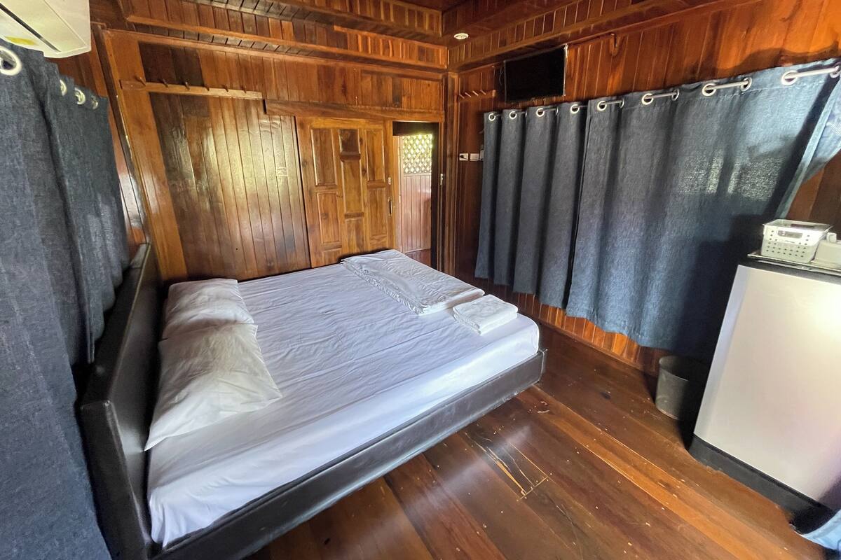 A wooden-paneled room with a bed, curtains, and a small white appliance.