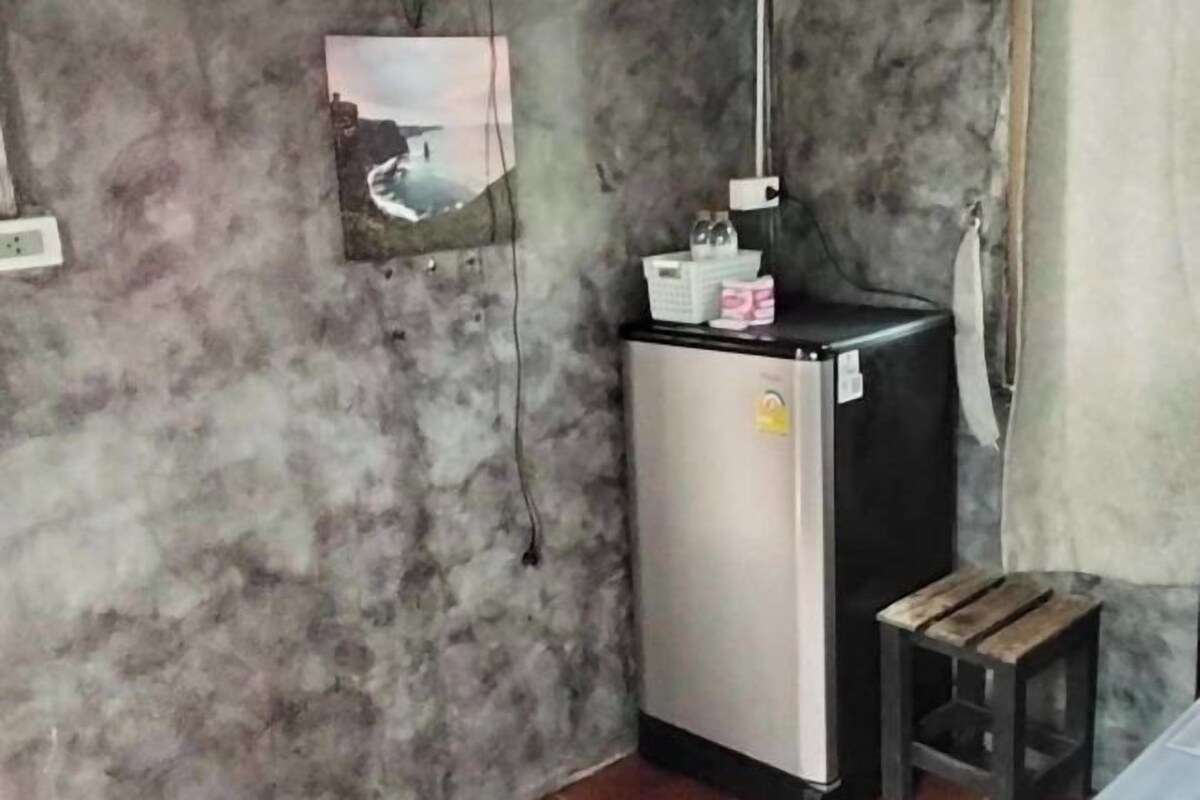 A small room with a marble-patterned wall, a refrigerator, a wooden stool, and a picture frame.