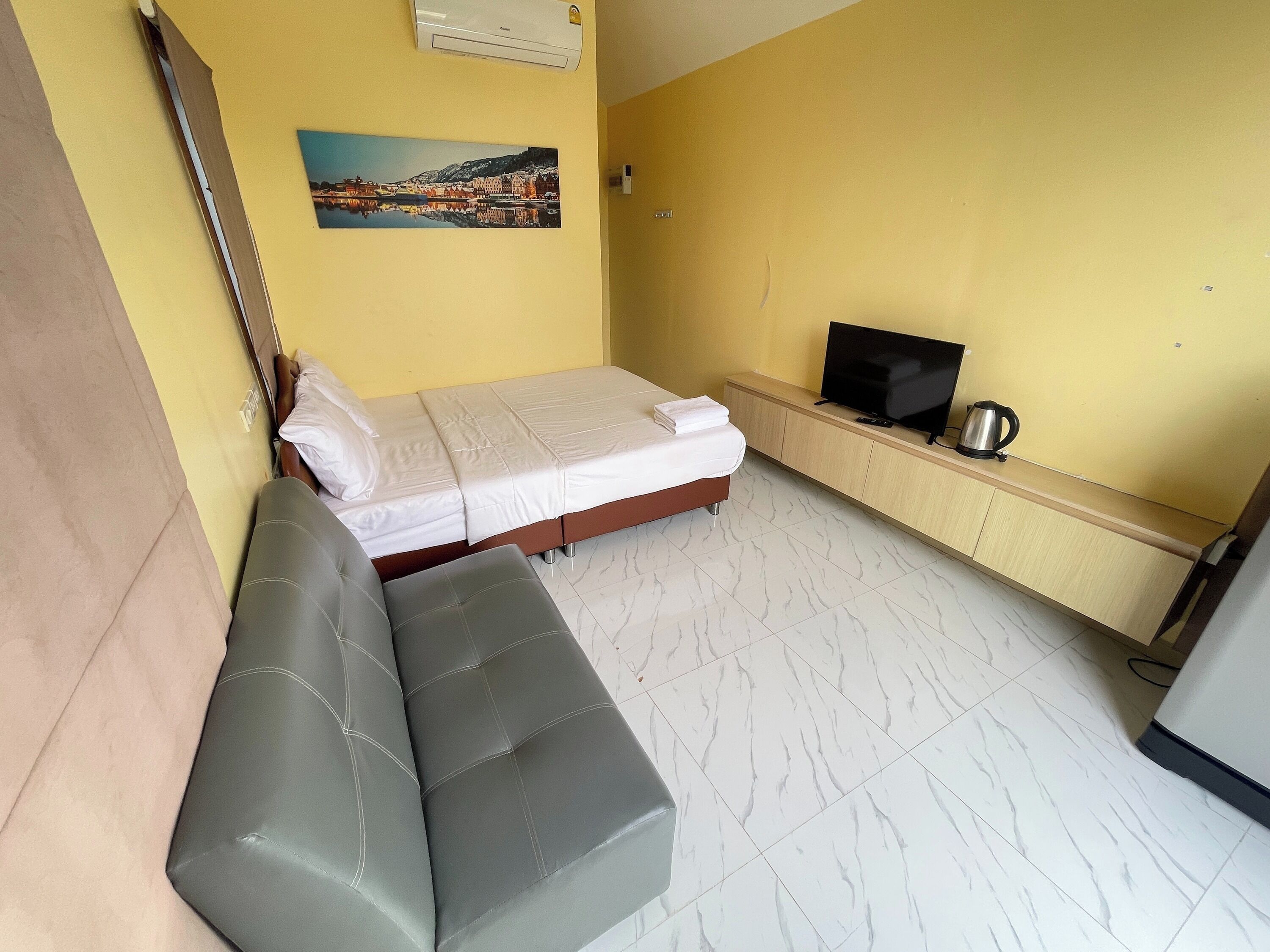 A small, compact room with a bed, a bench, a television, and a kettle on a shelf.