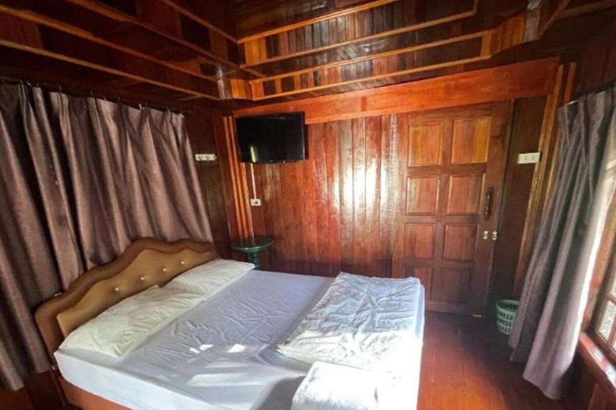 A wooden cabin room with a bed, curtains, a television, and a door.