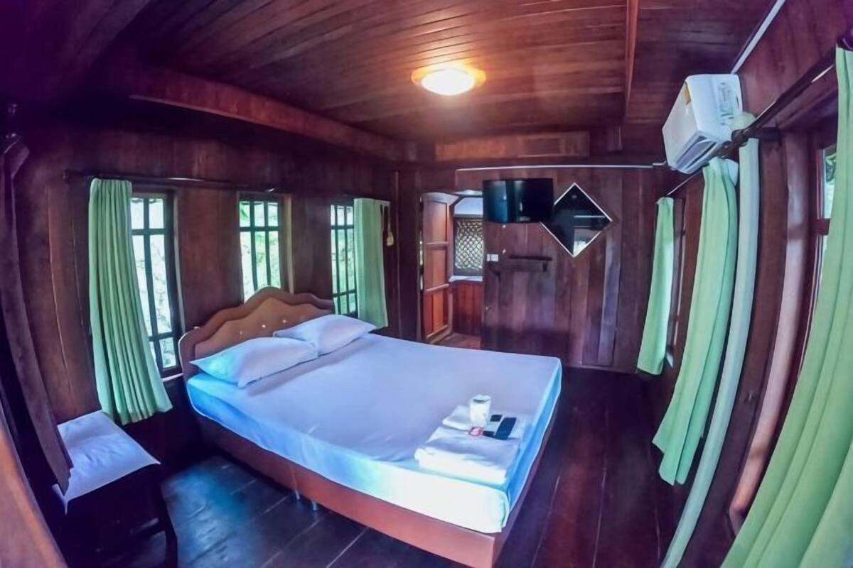 A wooden room with a bed, curtains, and a ceiling fan.
