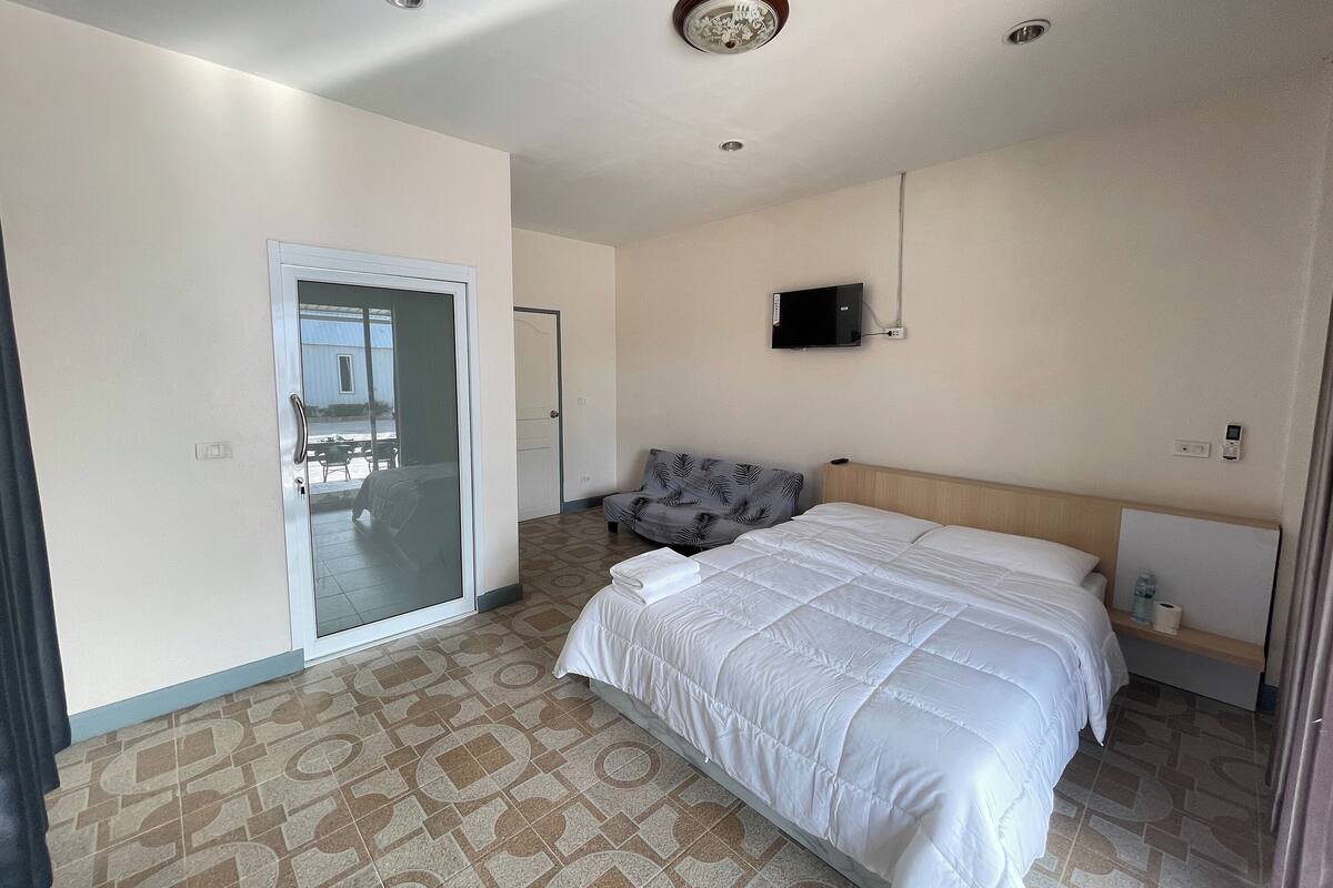 A hotel room with a bed, a TV mounted on the wall, a door leading to a balcony, and patterned floor tiles.