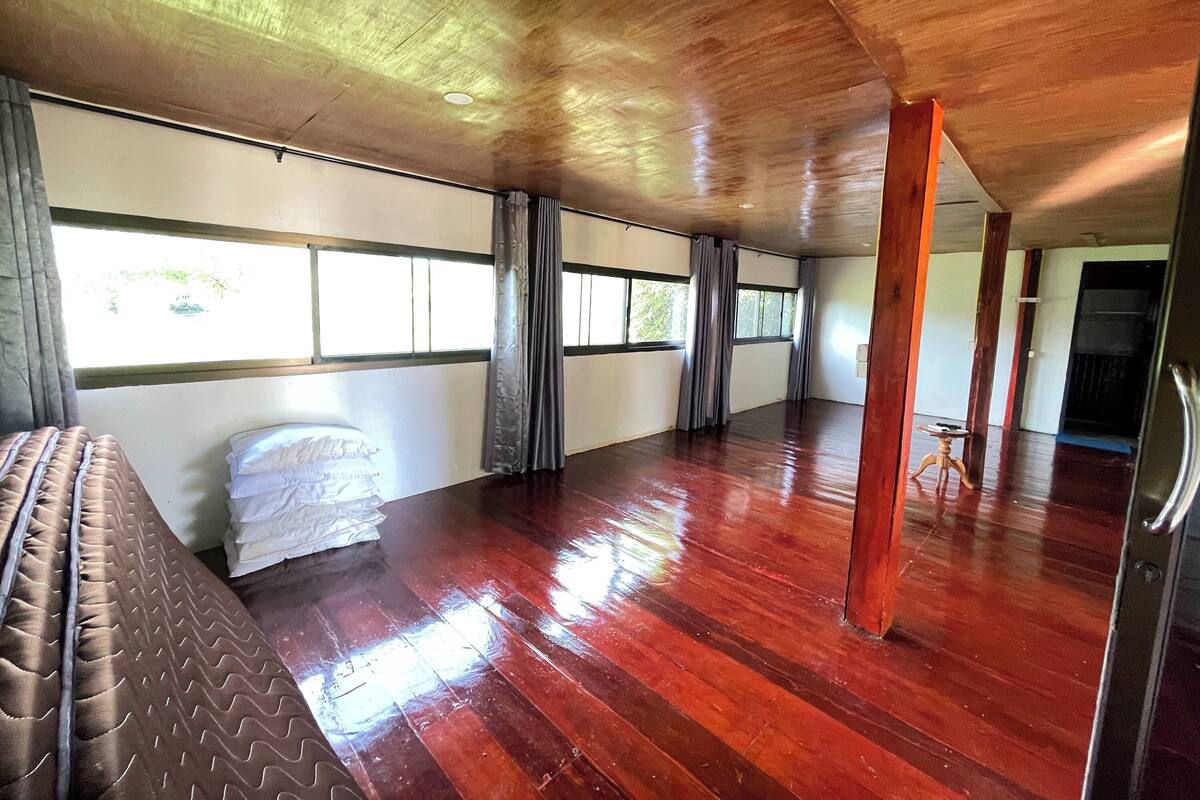 A spacious room with a wooden floor, a bed with a brown headboard, and a window with curtains.