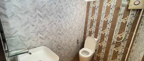 A bathroom with a herringbone tile pattern, a toilet, a shower with a handheld showerhead, and a glass-enclosed sink.
