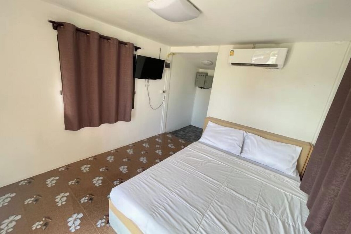 A single bed with white bedding, a television mounted on the wall, and an air conditioning unit.